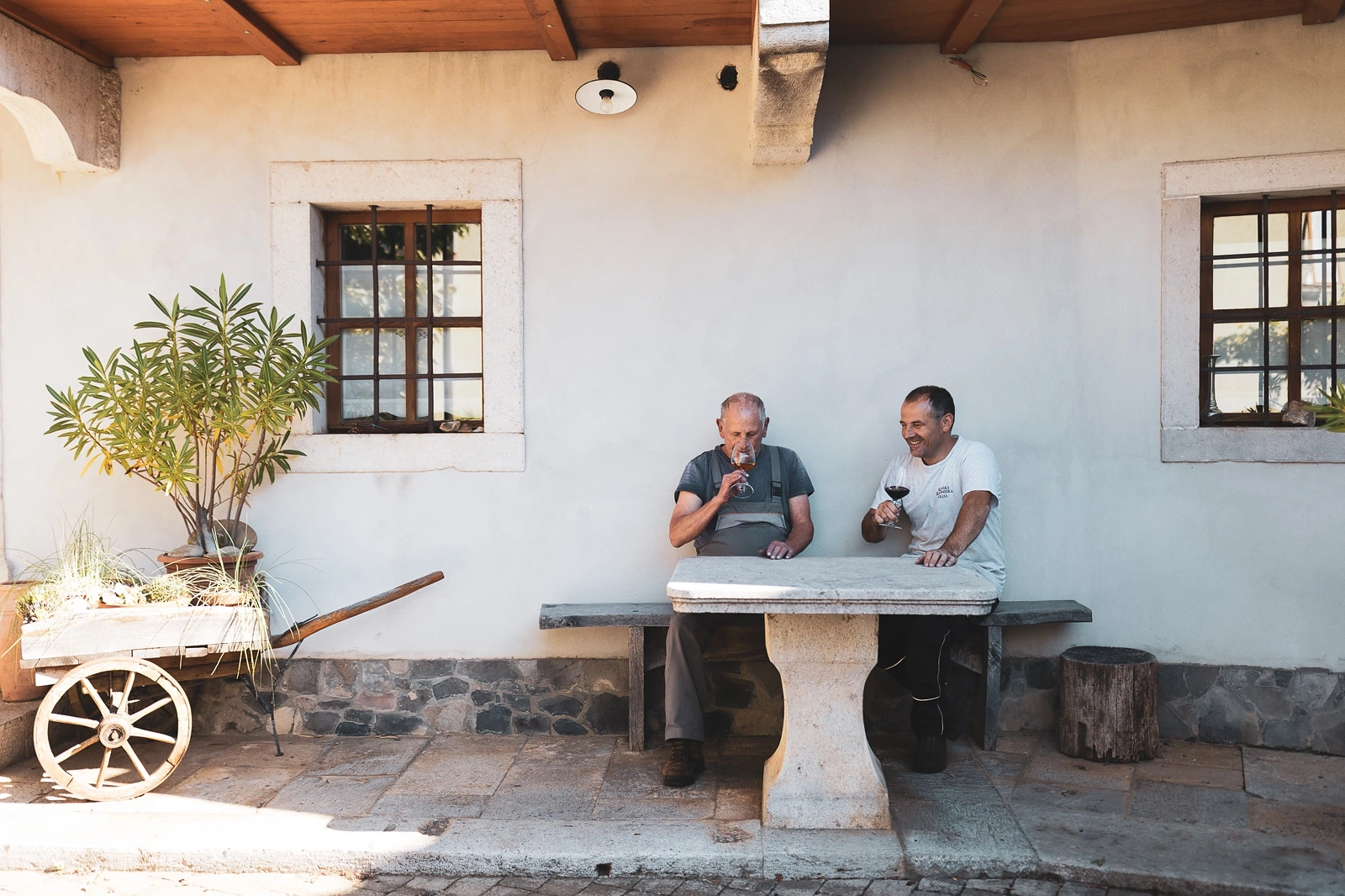 Emil and Rok at the stone table in front of the house, with a glass of wine